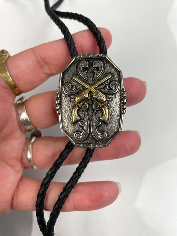 2-TONE ORNATE CROSSED PISTOL PLACARD BOLO TIE, BRAIDED LEATHER CORD
